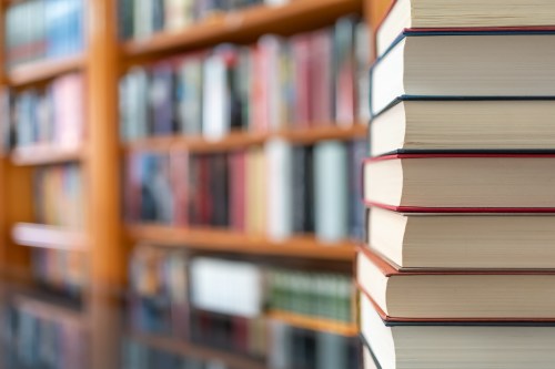 A stack of books in focus, with a blurred bookshelf in the background, creating a cozy reading atmosphere.