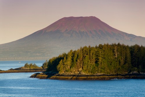 A serene landscape featuring a mountain with a purple peak, surrounded by lush greenery and calm waters.