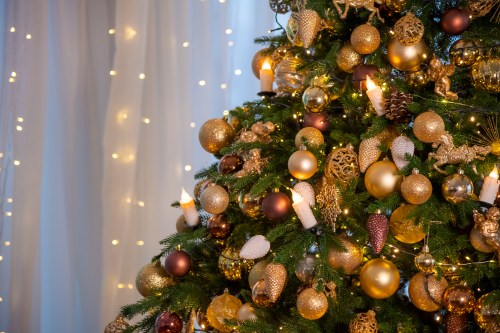 A beautifully decorated Christmas tree adorned with gold and bronze ornaments, candles, and twinkling lights.