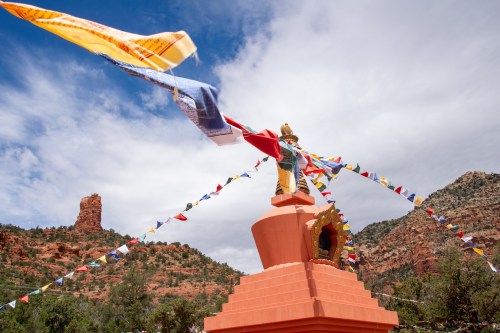 A colorful stupa with prayer flags against a backdrop of red rock formations and a cloudy sky.