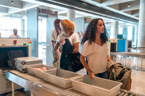 A group of people passing through a security checkpoint with luggage and personal items on a conveyor belt.