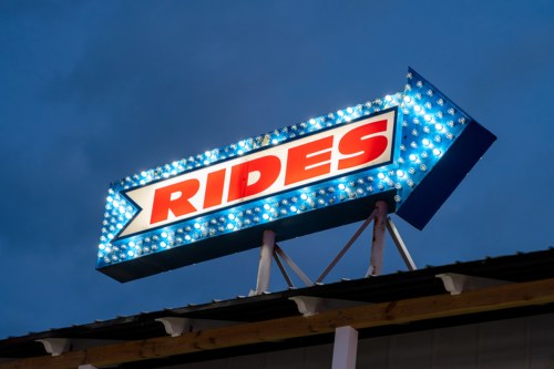 Brightly lit sign reading "RIDES" with an arrow, set against a twilight sky.