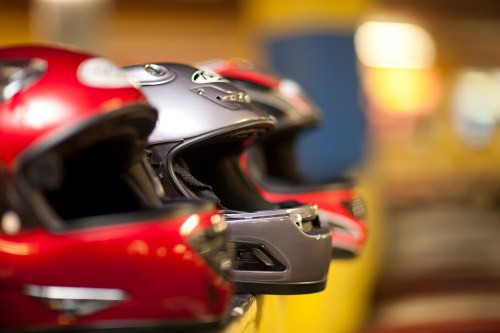A row of colorful racing helmets, including red and silver, displayed on a shelf in a vibrant indoor setting.
