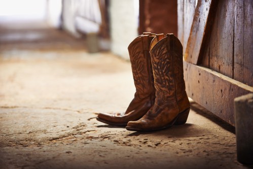 A pair of worn brown cowboy boots resting on a rustic barn floor near a wooden door.