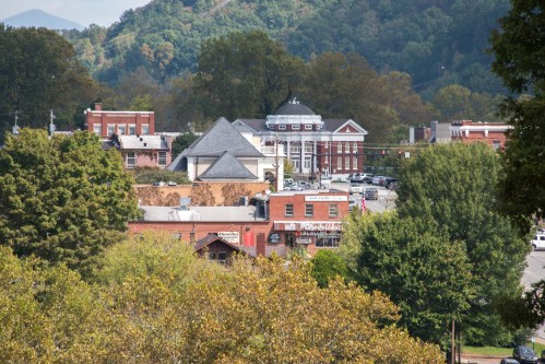 A scenic view of a small town with historic buildings, trees, and mountains in the background under a clear sky.