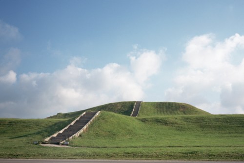 Two grassy mounds with staircases leading up, under a blue sky with scattered clouds.