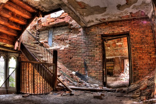 A dilapidated interior of a building with exposed brick walls, a staircase, and debris scattered on the floor.