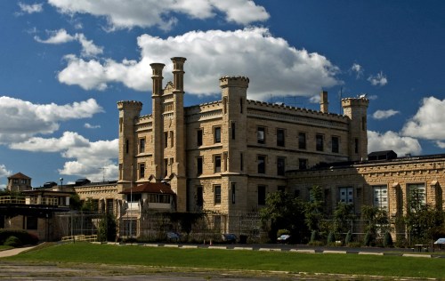 Historic stone building with towers, surrounded by greenery and under a blue sky with fluffy clouds.
