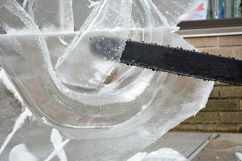 A close-up of a chainsaw cutting through a large block of ice, revealing intricate patterns and textures.
