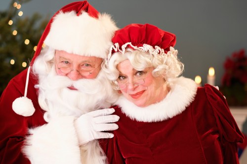 Santa Claus and Mrs. Claus pose together, both in festive attire, smiling warmly against a holiday backdrop.