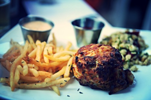 A plate with golden fries, a crab cake, and a side salad, accompanied by two small dipping sauces.