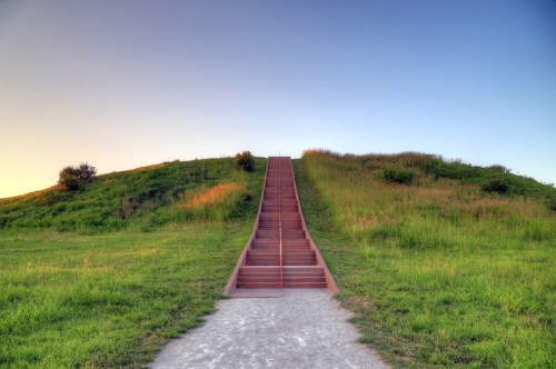A long staircase leads up a grassy hill under a clear sky at sunset.
