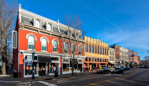 Historic buildings line a sunny street, showcasing a mix of architectural styles and storefronts.