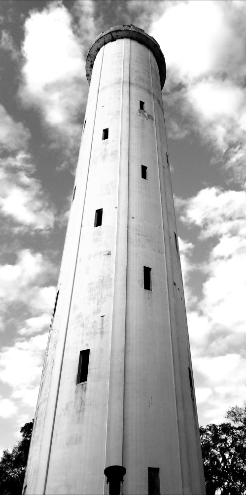 A tall, cylindrical water tower against a cloudy sky, captured in black and white.