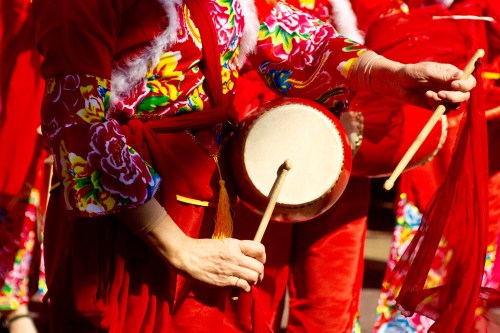 A close-up of hands playing a drum, adorned in vibrant red clothing with floral patterns.