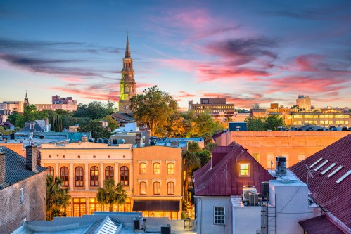 A vibrant sunset over a historic cityscape, featuring colorful buildings and a church steeple against a dramatic sky.