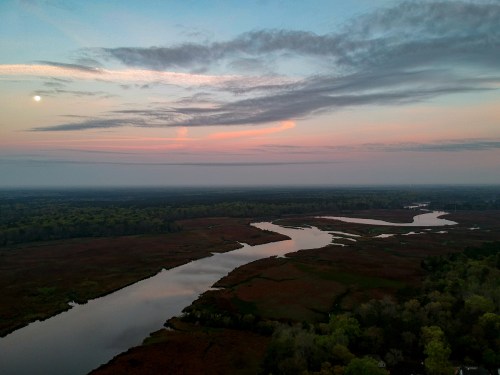 A serene landscape at dusk, featuring a winding river, lush greenery, and a soft pink and blue sky with clouds.
