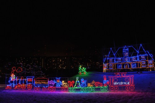 Colorful holiday lights form a train and a house, creating a festive scene against a dark night sky.