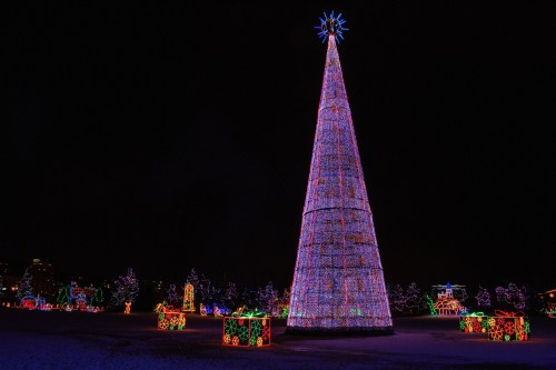 A brightly lit Christmas tree surrounded by colorful gift boxes, set against a dark night sky.