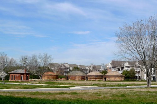 Historic brick structures with domed roofs, surrounded by grass and residential buildings under a blue sky.