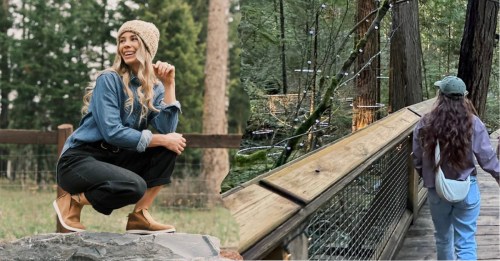A woman squats on a rock in a forest, while another walks on a wooden path surrounded by trees and lights.