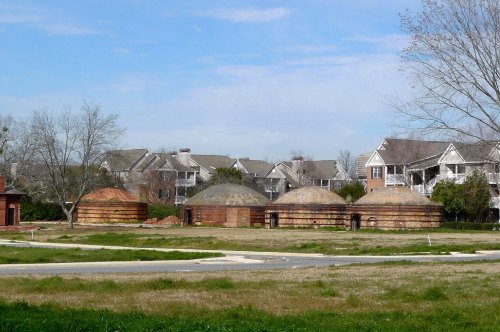 A row of dome-shaped structures in a grassy area, with residential buildings in the background under a clear blue sky.