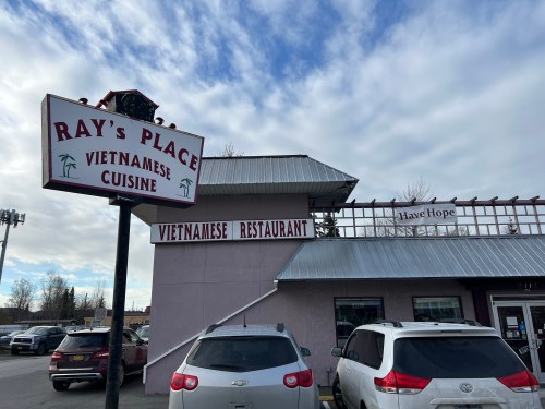 Sign for Ray's Place Vietnamese Cuisine, a restaurant with a pink exterior and parked cars in front.