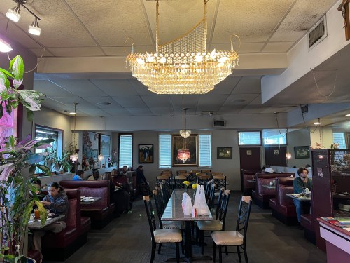 A cozy restaurant interior with booths, tables, and a chandelier, featuring diners enjoying their meals.