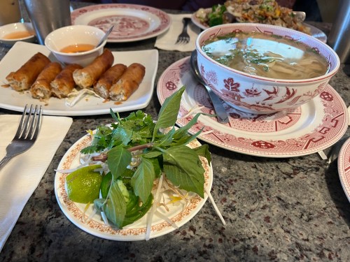 A table setting with spring rolls, a bowl of soup, and a plate of fresh herbs and lime.