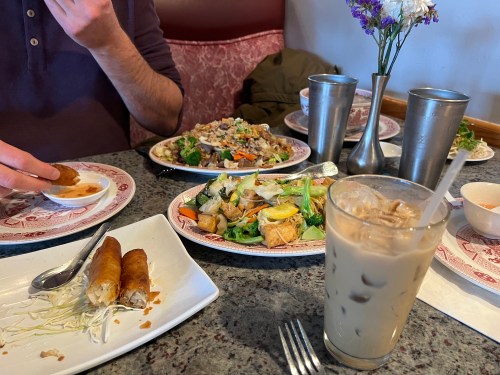 A table with various dishes, including spring rolls, a stir-fry, and a glass of iced coffee.
