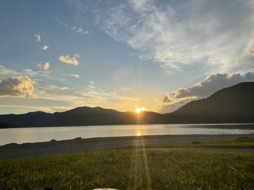 Sunset over a calm lake, with mountains in the background and a colorful sky filled with clouds.