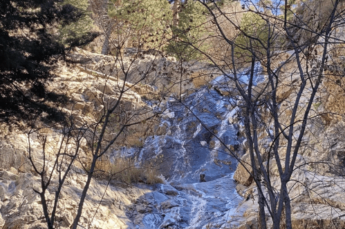 A small waterfall cascades over rocky terrain, surrounded by trees and dry foliage.