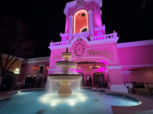 A brightly lit building with a pink facade and clock tower, featuring a fountain in front at night.