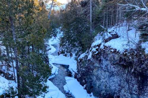 A snowy landscape with a winding river surrounded by trees and rocky cliffs.