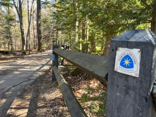 A wooden fence along a path in a forest, with a sign for North Country Scenic Trails visible.