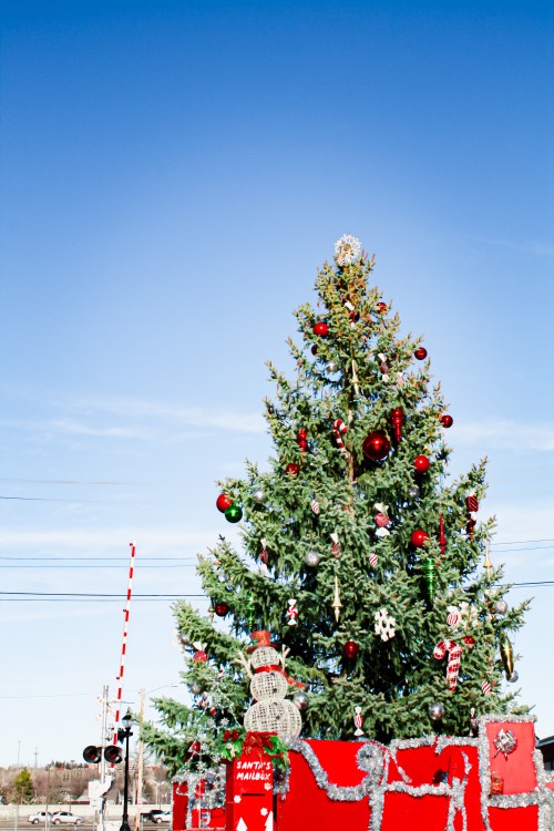 A decorated Christmas tree with ornaments and a snowman sits in front of a clear blue sky.