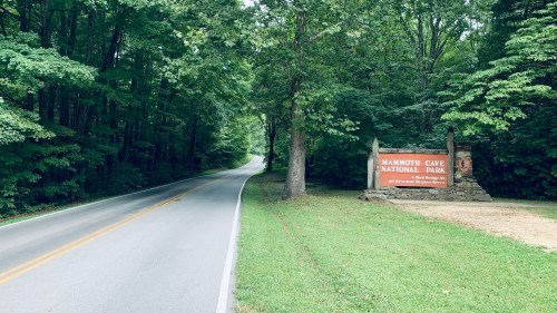 A winding road leads to the entrance of Mammoth Cave National Park, surrounded by lush green trees.