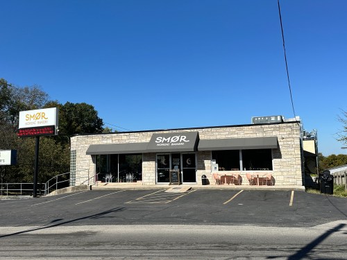 Exterior of SMØR Nordic Bakery, featuring a stone facade and outdoor seating, under a clear blue sky.