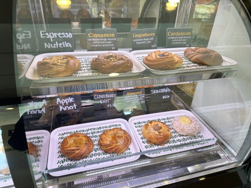 Display case with various pastries: cinnamon, lingonberry, cardamom, apple knot, cloudberry, and skullberry knots.