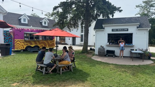 A food truck and outdoor seating area with people enjoying food under umbrellas in a grassy space.