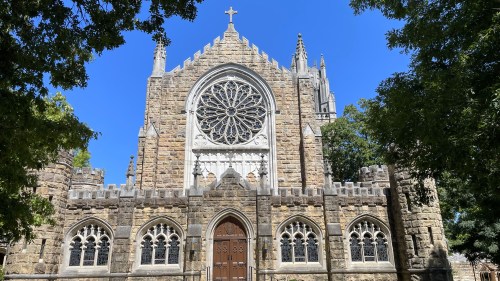 A stone church with a large rose window, intricate architecture, and a clear blue sky in the background.