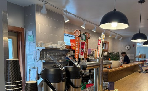 A cozy café interior with coffee taps, a counter, and a barista preparing drinks under warm lighting.