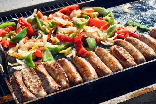 Grilled sausages and colorful bell peppers and onions sizzling on a barbecue grill.
