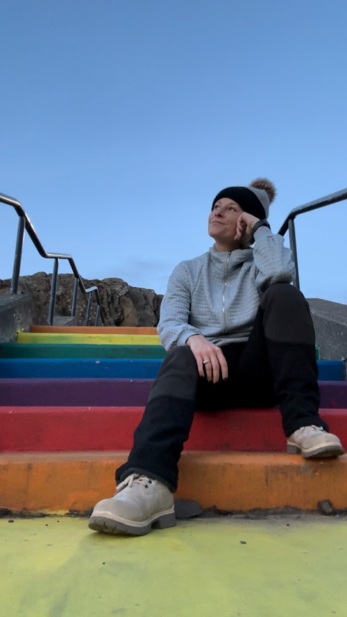 A person sits on colorful stairs, resting their chin on their hand, looking thoughtfully into the distance.