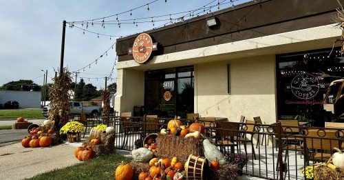 A cozy coffee shop adorned with pumpkins and fall decorations, featuring outdoor seating and string lights.