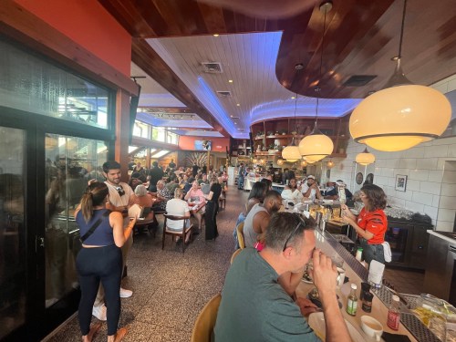 A bustling restaurant interior with diners, a bar area, and warm lighting, creating a lively atmosphere.