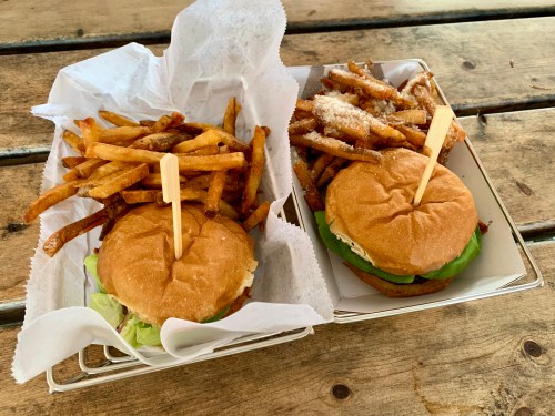 Two burgers with lettuce and toppings, served with a side of crispy fries on a wooden table.