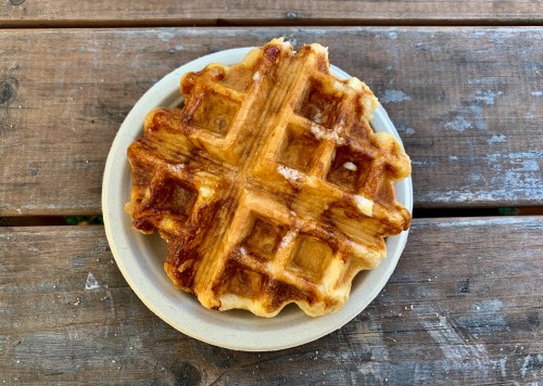 A golden-brown waffle on a beige plate, resting on a rustic wooden table.