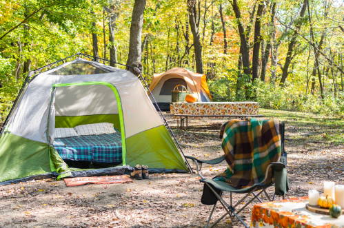 A cozy campsite with two tents, a picnic table, and a chair surrounded by colorful autumn trees.