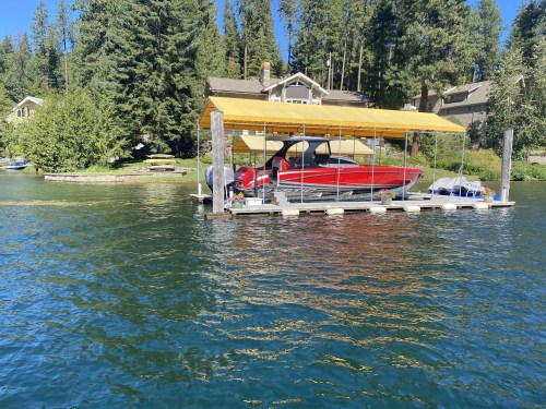 A red boat under a yellow canopy on a dock, surrounded by trees and a house in the background.